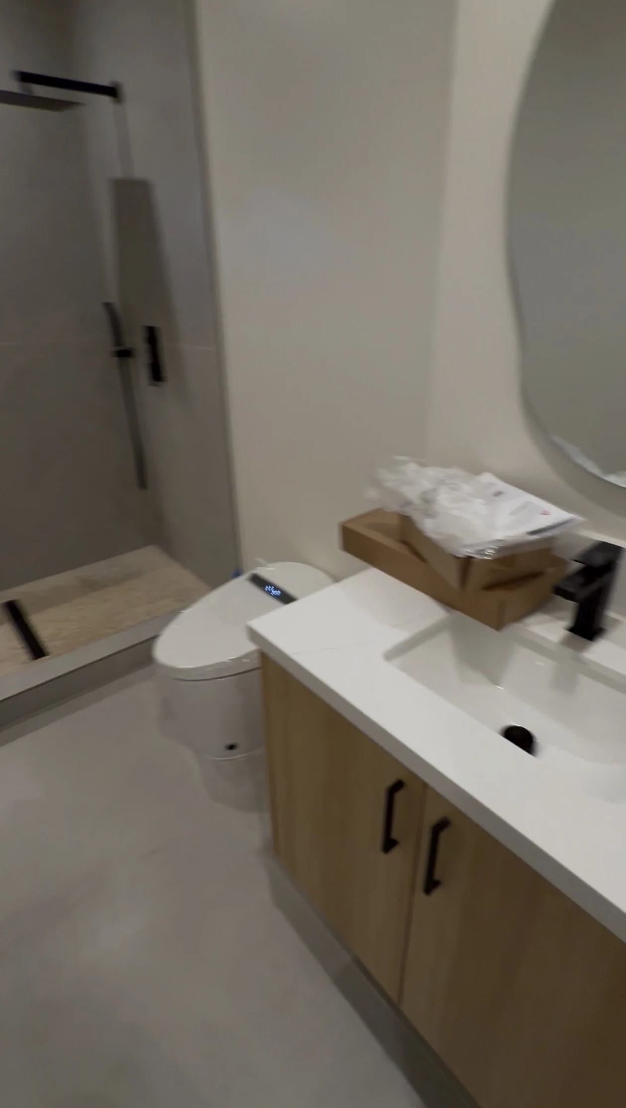 The ADU bathroom with a tiled shower, toilet, wood vanity, white counter and round mirror.