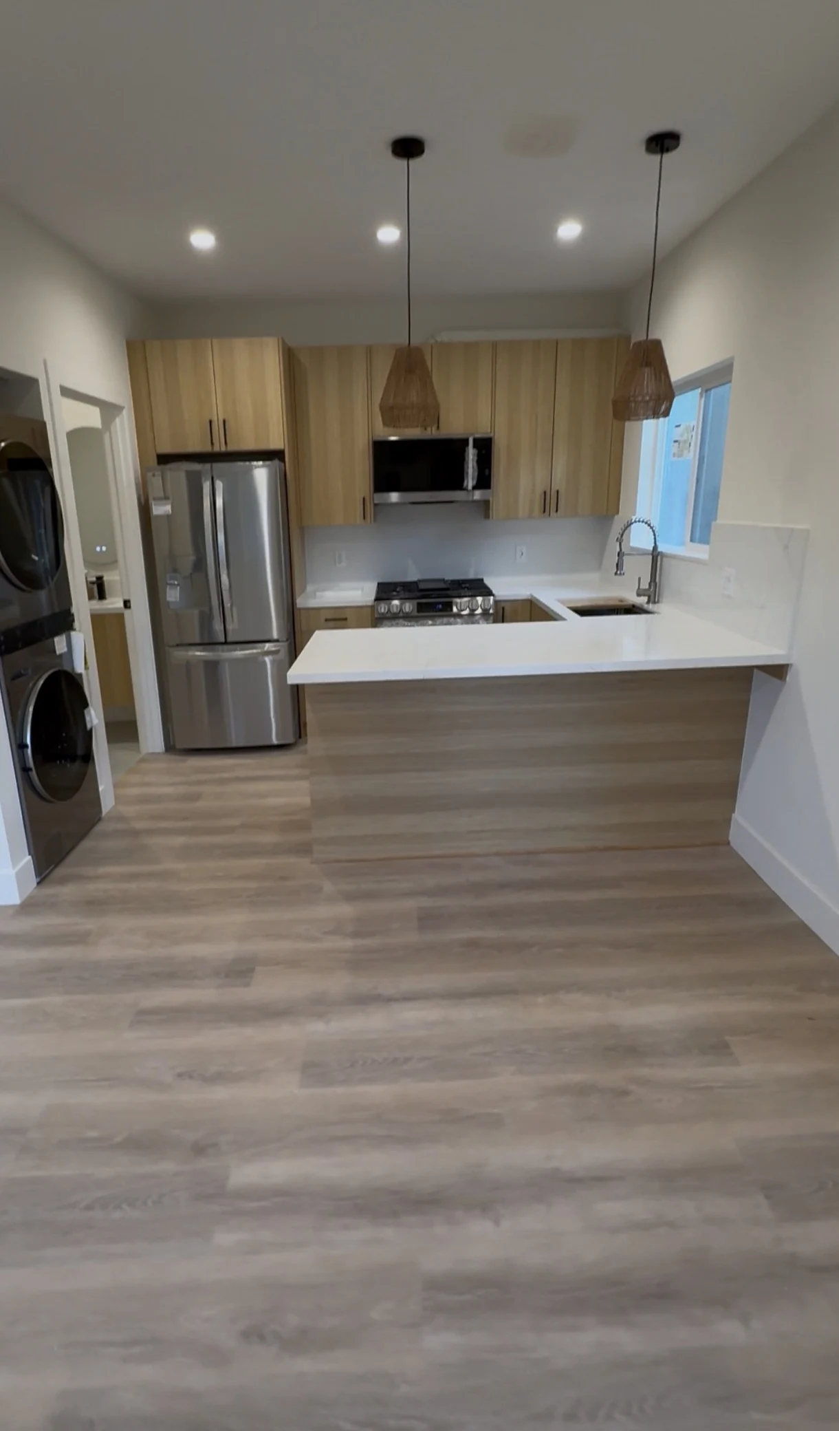 Wood cabinetry, white counters, a peninsula and two woven pendants in the finished ADU kitchen.