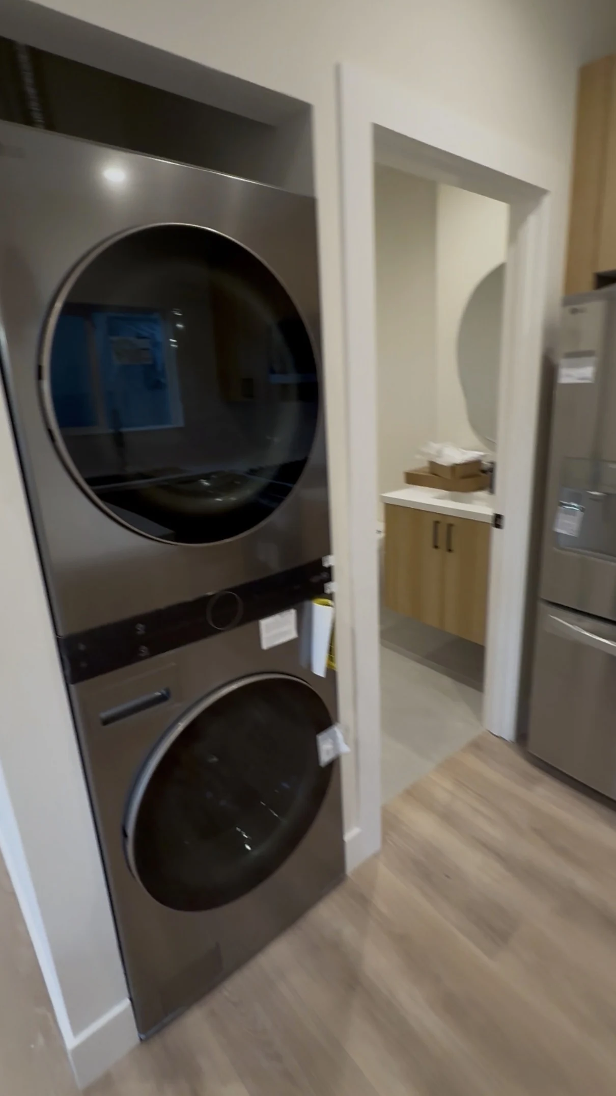 Stacked laundry appliances beside the bathroom doorway and refrigerator in the ADU.