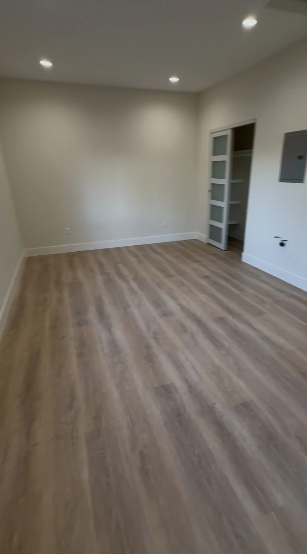 An empty ADU living area with wood-tone flooring, recessed lighting and a sliding closet door.