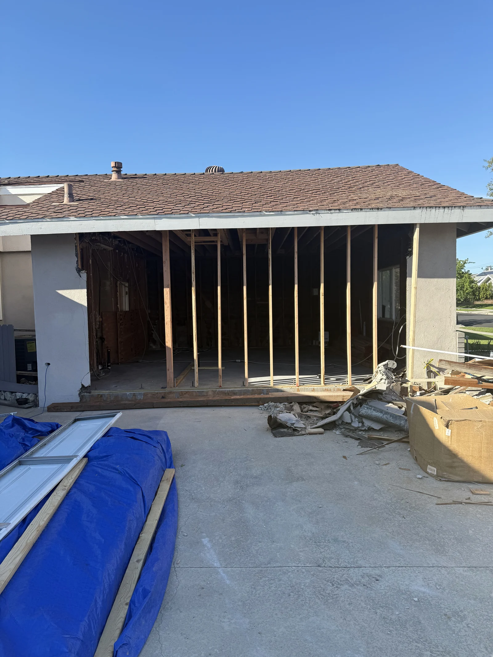 An exterior opening with new vertical framing, existing roof and construction materials in the foreground.